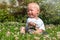 Happy little boy sits in a field of green grass and flowers