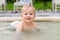 Happy little caucasian blond toddler boy swimming in wading pool on bright summer day at resort. Adorable baby enjoying outdoor