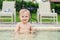 Happy little caucasian blond toddler boy swimming in wading pool on bright summer day at resort. Adorable baby enjoying outdoor