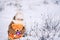 Happy little caucasian girl sitting on the snow and holding an orange teddy bear