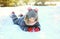 Happy little child lying playing on snow in winter