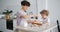 Happy little child rolling dough with mother at kitchen table in apartment