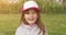 Happy little cute girl in trucker cap smiling and looking at camera while standing in summer garden