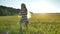 Happy little daughter with long blonde hair running and hugging her mother, smiling, beautiful wheat field during sunset