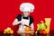 Happy little girl in chef uniform cuts fruit in kitchen