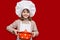 Happy little girl in chef uniform holds saucepan isolated on red. Kid chef