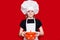 Happy little girl in chef uniform holds saucepan isolated on red. Kid chef. Cooking Concept