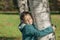 Happy little girl with closed eyes, hugging a birch trees in autumn park and enjoying her leisure time on sunny warm day