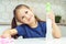 Happy little girl with detergent sprayer and household rag at table. Portrait of child tidying up kitchen, home cleaning