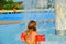 Happy little girl enjoying summer day in the swimming pool. Girl going to a sprinkler in spray pool. Cute girl with inflatable ar