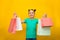 Happy little girl with funny tails standing isolated over yellow background holding shopping bags. Looking camera