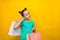 Happy little girl with funny tails standing isolated over yellow background holding shopping bags. smiles thoughtfully