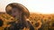 A happy little girl in the hat is smiling at the field of sunflowers at sunset time.