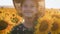 A happy little girl in the hat is smiling at the field of sunflowers at sunset time.