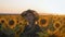 A happy little girl in the hat is smiling at the field of sunflowers at sunset time.