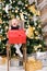 Happy little girl holding wrapped present sitting beside decorated christmas tree at home on boxing day