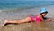 A happy little girl lying on the beach in the sea among waves and relax in summer. Kid is playing with sand. Girl is