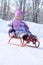 Happy little girl in pink scarf and hat goes tobogganing
