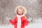 A happy little girl in a red suit is standing under falling snow in the forest. A child plays on a winter walk in the fresh air