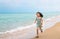 Happy little girl is running along the beautiful beach, motion blur, smiling face, wearing cute dress, black long hair, 7 years