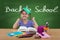 Happy little girl in the school bench, behind Back To School sign on the blackboard