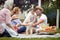 Happy little girl sitting in dad`s lap, surrounded by family at picnic. love and affection, joy concept