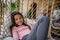 Happy little girl sitting in wicker rattan hang chair outdoors in patio in autumn, looking at camera