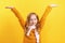 Happy little girl in a sweater and scarf on a yellow background. The child raised his hands up. Concept for autumn, holiday, sale.