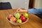 Happy little girl takes a pear from the bowl with variety fruits on table at home