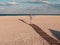 Happy little girl walking alone on wooden boardwalk on seascape background blue sky. Child resting running on sand beach