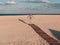 Happy little girl walking alone on wooden boardwalk on seascape background blue sky. Child resting running on sand beach