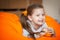 Happy little girl wallows in an orange bean bag chair with a ripe orange fruit