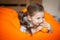 Happy little girl wallows in an orange bean bag chair with a ripe orange fruit