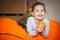 Happy little girl wallows in an orange bean bag chair with a ripe orange fruit