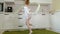 A happy little girl in a white gymnastic swimsuit trains, dances with a ribbon for rhythmic gymnastics, jumps and