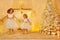 Happy Little Girls Playing Next to Christmas Tree with Gifts in White Home Room Interior with Fireplace Candles and Golden Xmas
