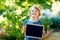 Happy little kid boy with chalk desk in hands. Healthy adorable child outdoors Empty desk for copyspace holding by