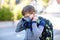 Happy little kid boy with glasses, medical mask and backpack or satchel. Schoolkid on way to school. Healthy adorable