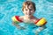 Happy little kid boy having fun in an swimming pool. Active happy preschool child learning to swim. with safe floaties