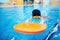 Happy little kid girl learning to swim with pool board with coach woman
