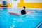 Happy little kid girl learning to swim with pool board with coach woman