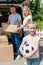 happy little kid holding soccer ball while her parents unpacking cardboard boxes