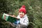 Happy little smiling girl in red cap with Christmas gift box standing near by spruce. Holiday celebrate concept