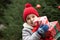 Happy little smiling girl in red cap with Christmas gift boxes standing near by spruce. Holiday celebrate concept