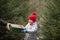 Happy little smiling girl in red cap takes a given box with a gift for Christmas. Kid standing near by spruce. Holiday celebrate