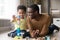 Happy little son playing with black dad using wooden blocks