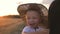 Happy little toddler boy in hat having fun sitting in parents arms in field in summer at sunset. Happy childhood concept