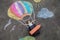 Happy little toddler girl flying in hot air balloon painted with colorful chalks in rainbow colors on ground or asphalt