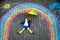 Happy little toddler girl in rubber boots with rainbow sun and clouds with rain painted with colorful chalks on ground