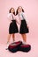 Happy little twin schoolgirls posing in uniform. Low angle. Over pink